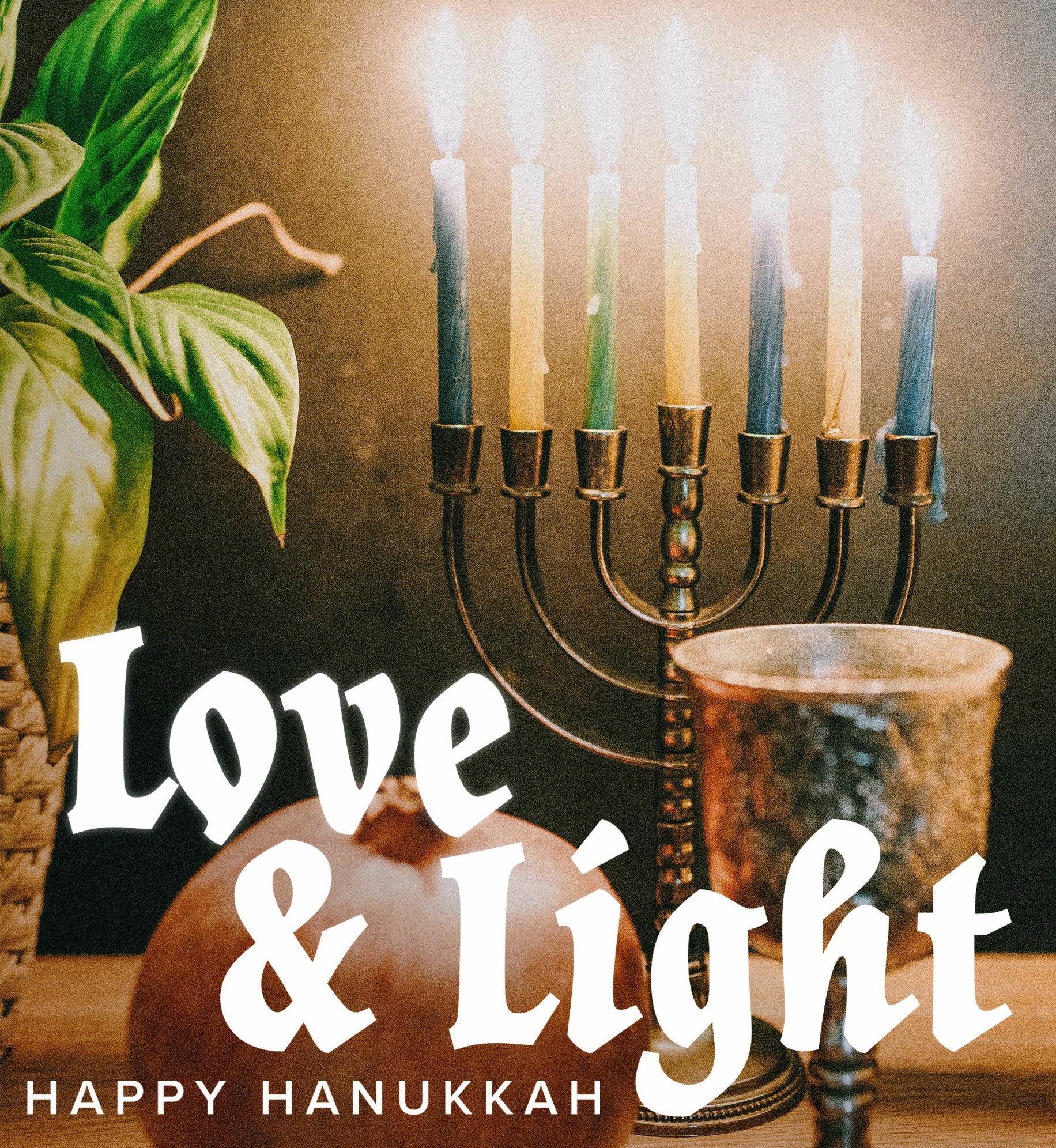 Menorah on table with pomegranate and goblet. Text: Love & light. Happy Hanukkah.