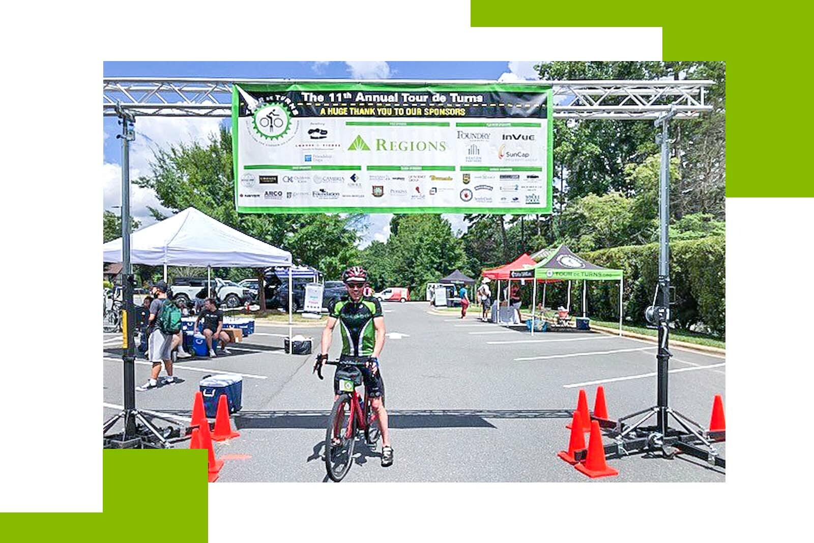 smiling man on a bicycle at a finish line