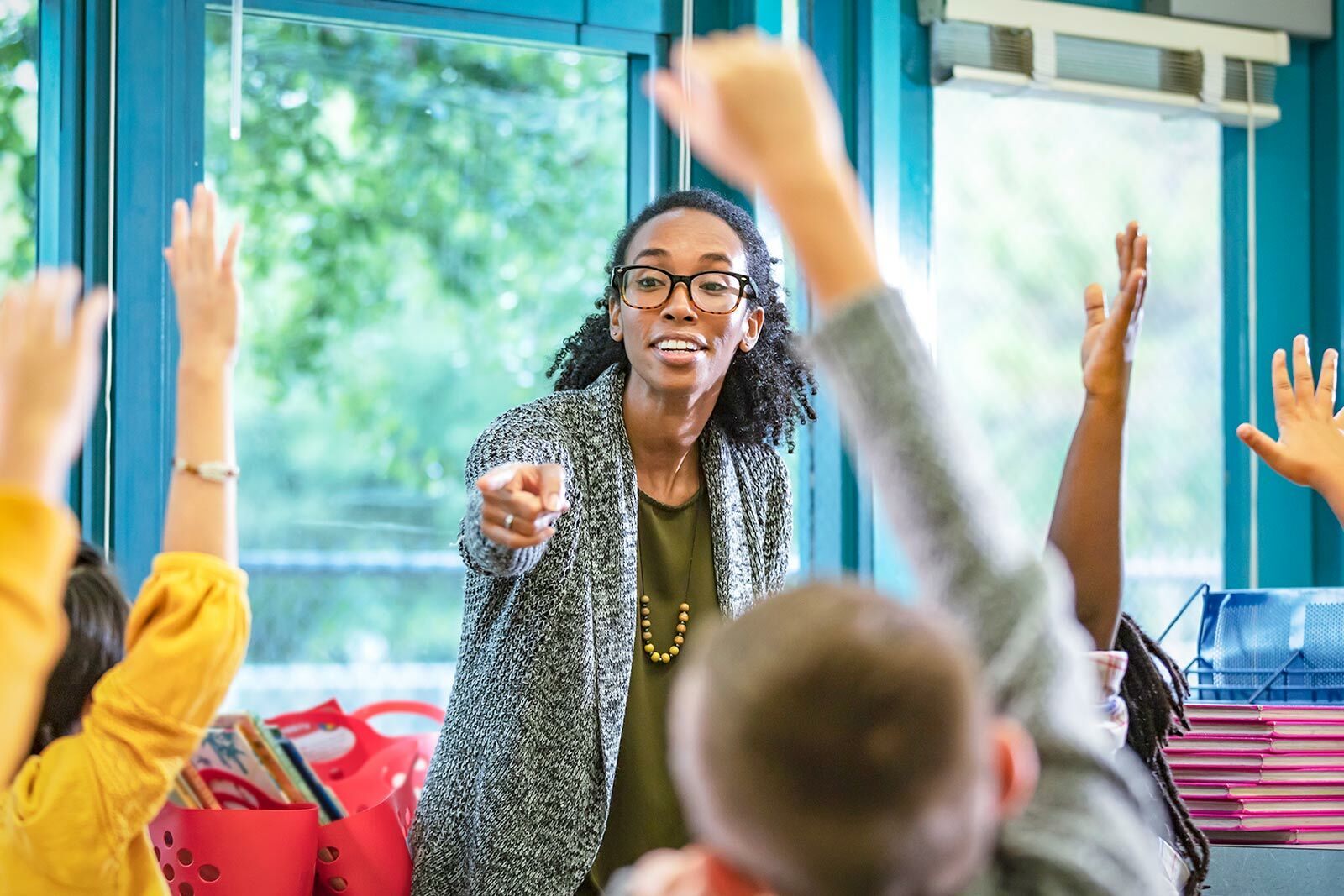 Teacher in a classroom with students raising their hands.
