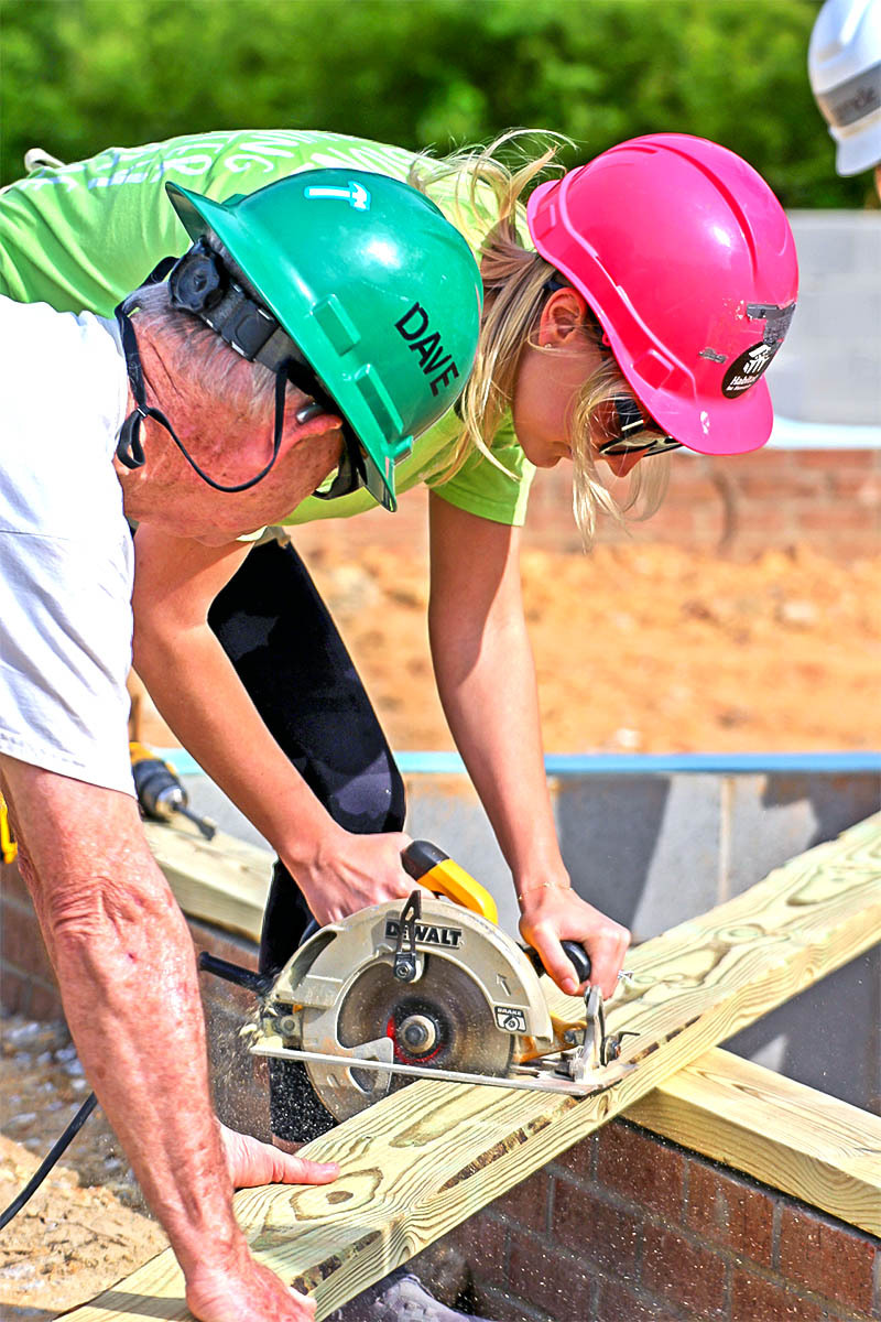 a volunteer from Regions bank being guided in sawing a board