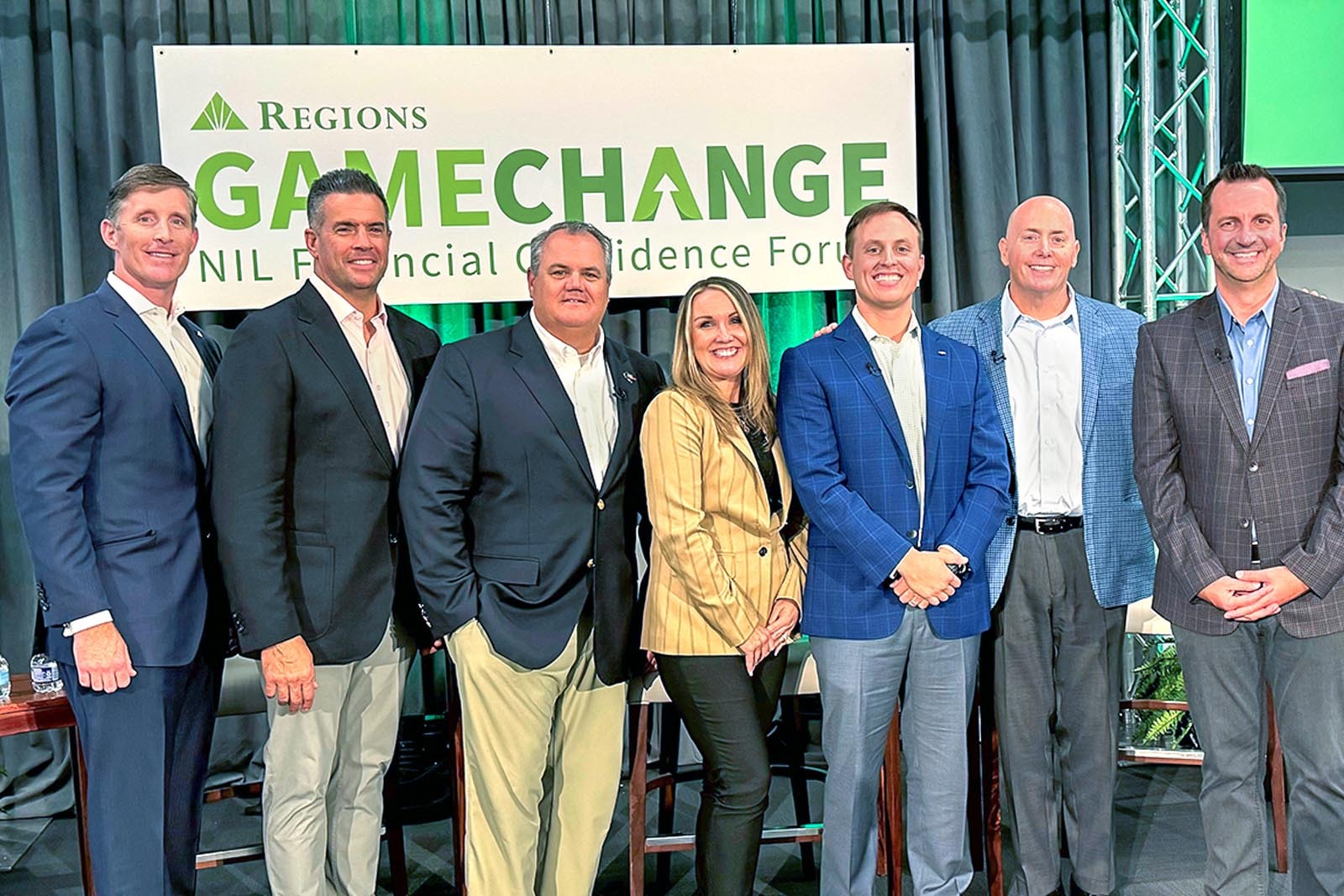 Group of panelists standing in front of Regions Game Change NIL banner.
