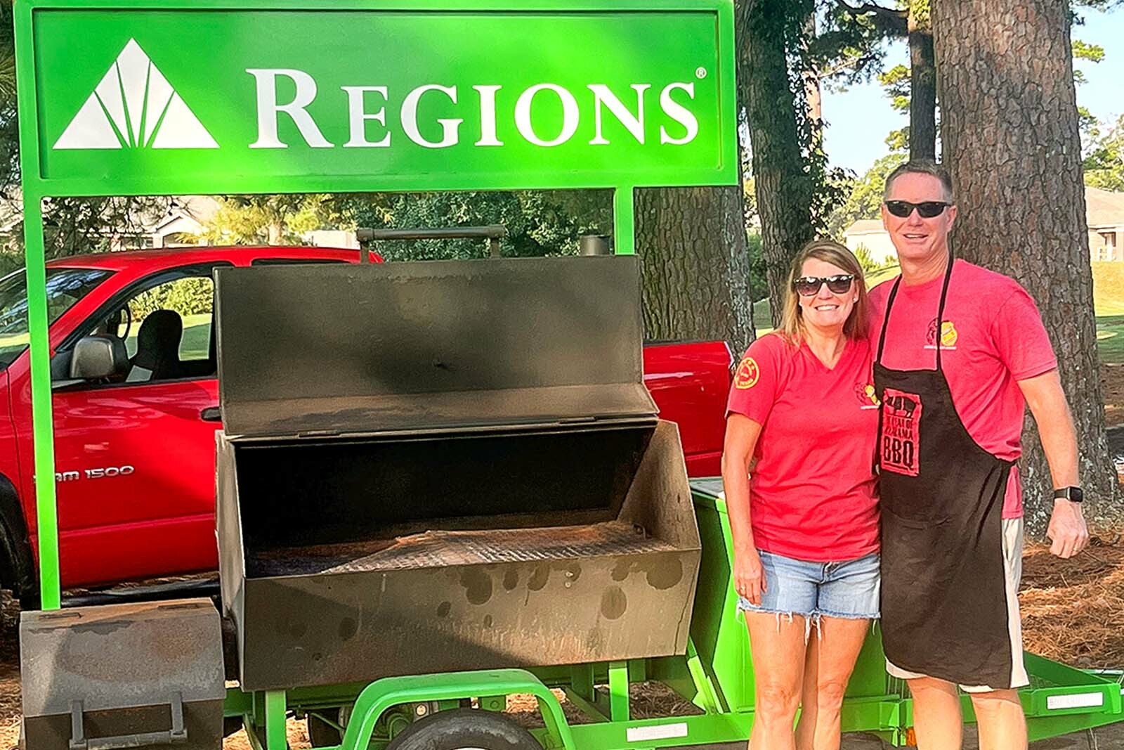 Steve Brown and Kara Newman standing next to the grill and Regions logo sign.
