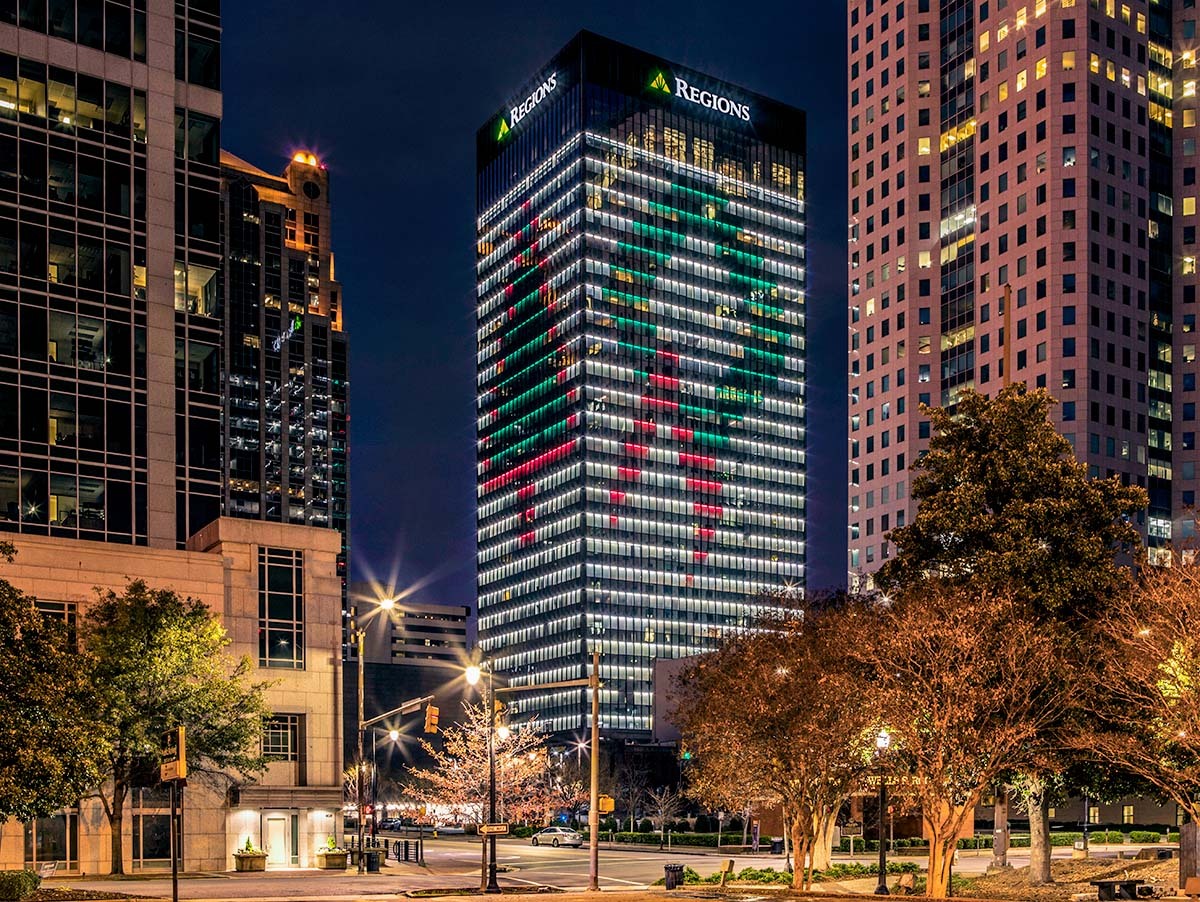Regions center at night with two sides of the building lit up in a Christmas motif. One side is a tree and the other is a wreath.