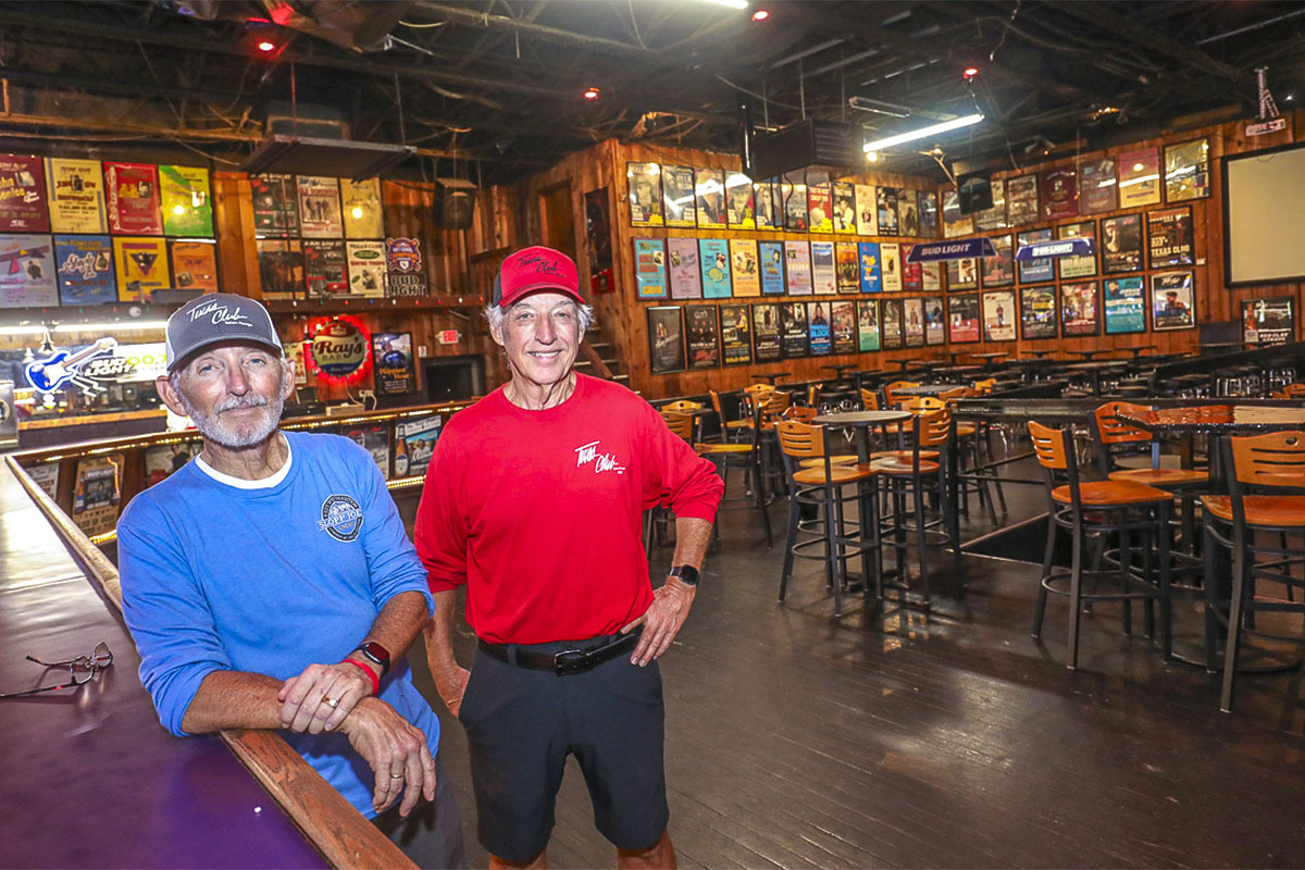 Brothers Mark and Mike Rogers stand next to the bar of the popular Texas Club. In the background, the wall is lined with posters of many of the famous acts that have performed at the venue.