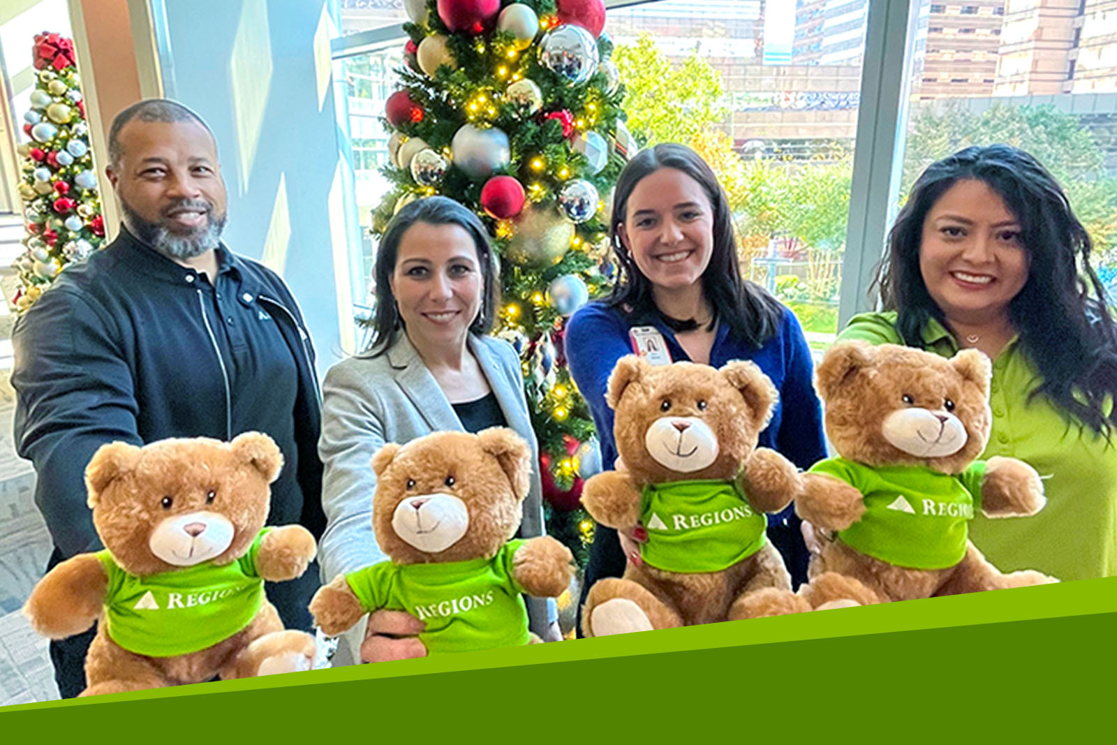 Four smiling people standing in front of a Christmas tree,...
