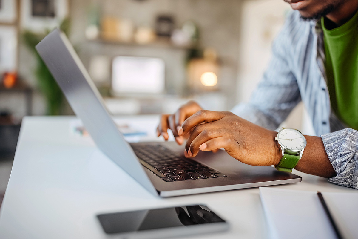 Man typing on a laptop with cell phone on table.