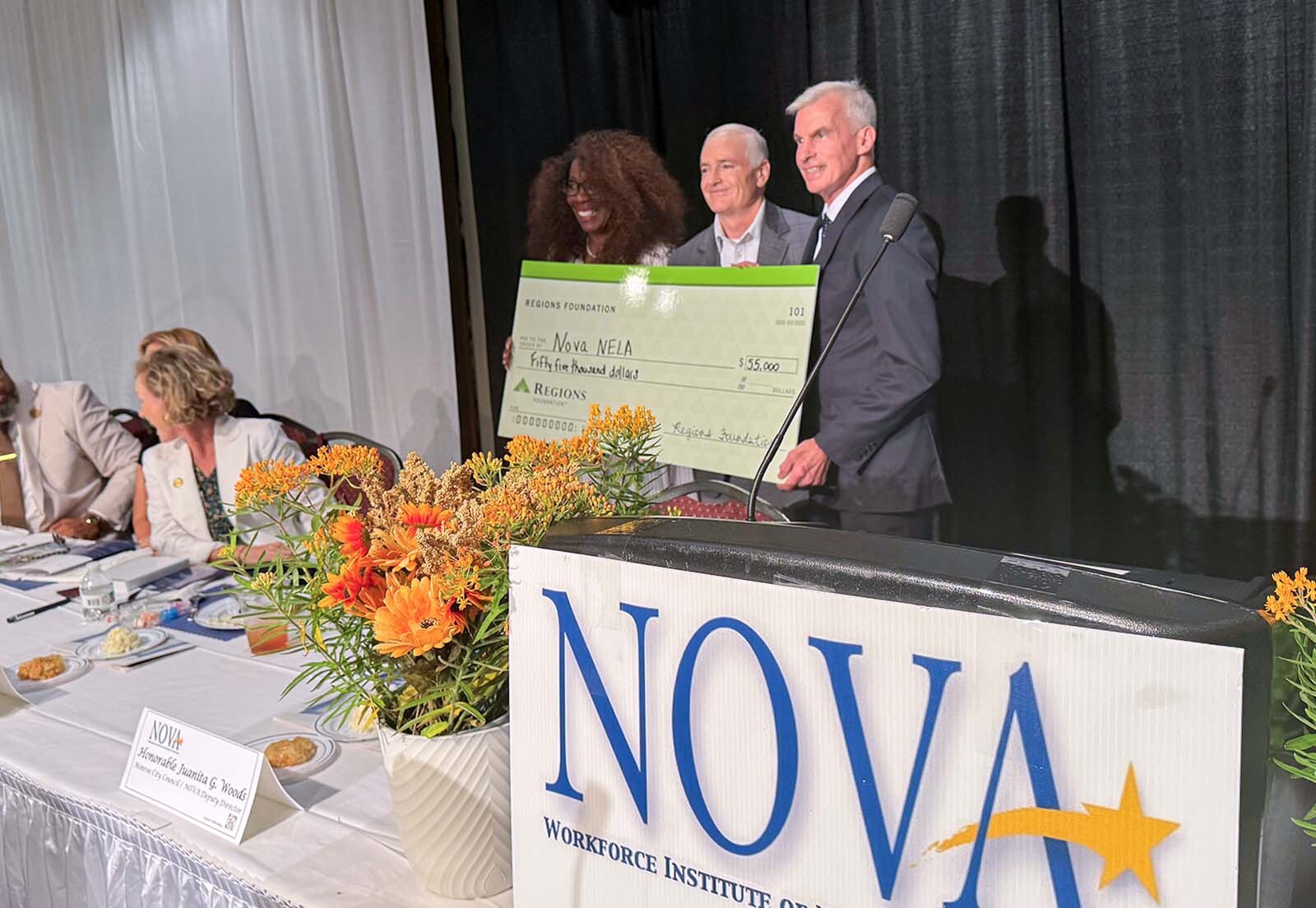 3 person group photo of check presentation at the NOVA panelist table.