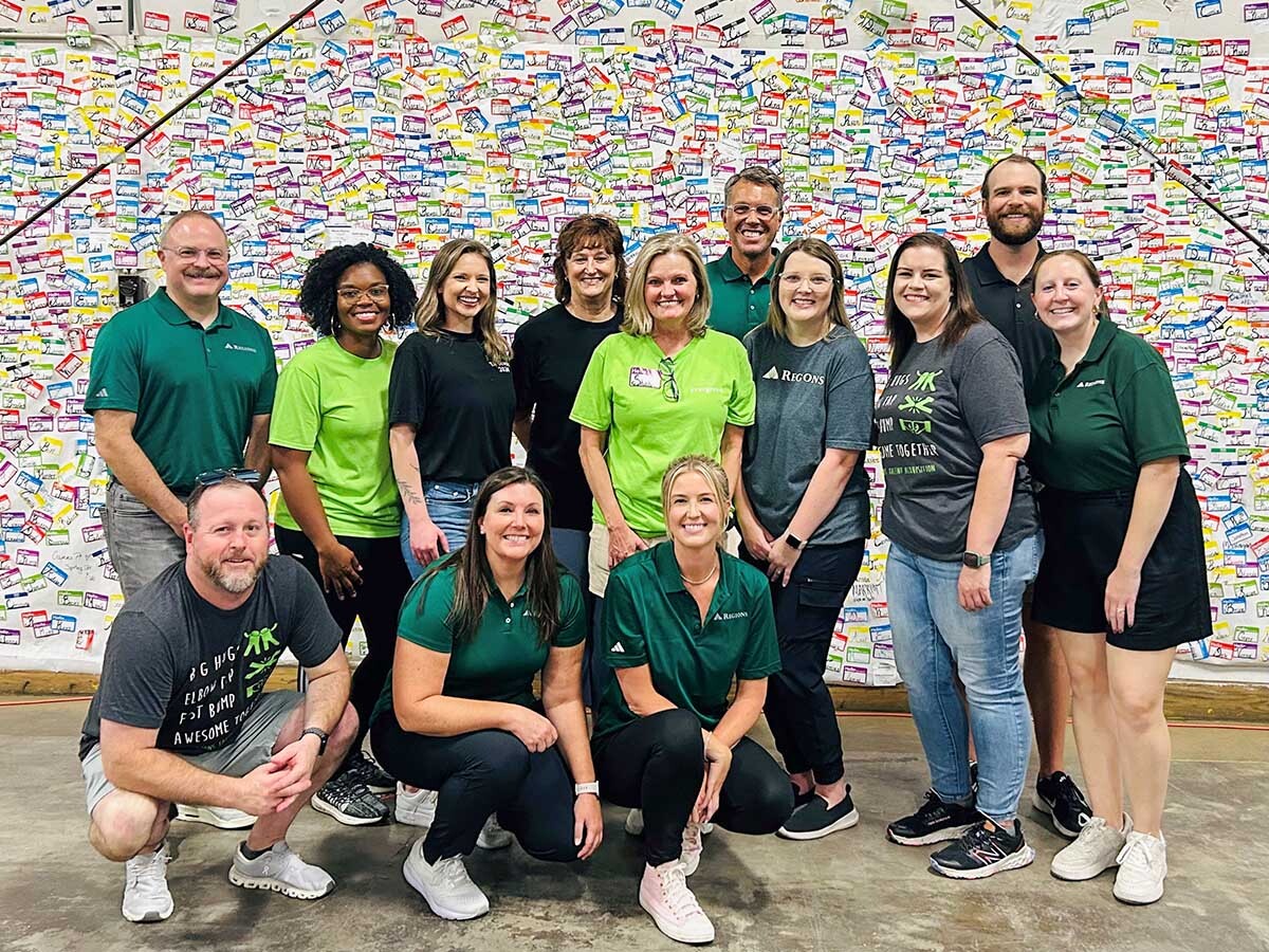 Group Photo of Regions Volunteers in Front of a nametag wall at TA Food Bank