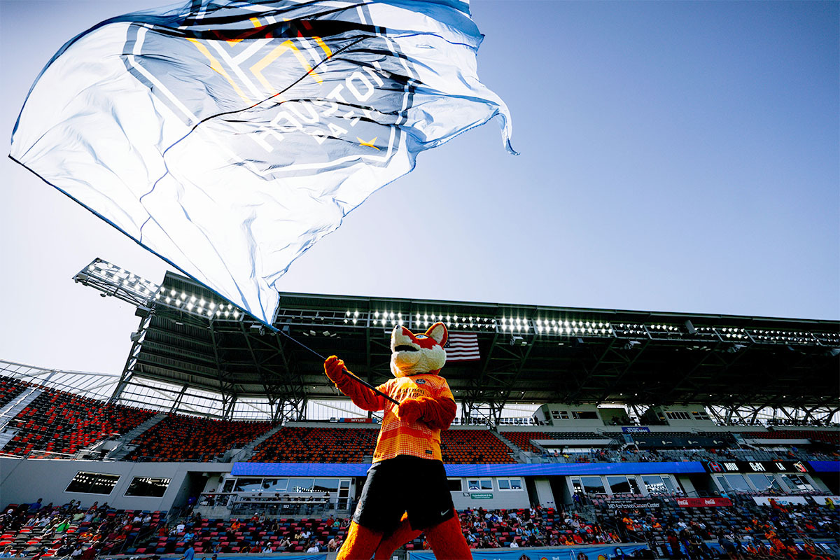 Dramatic photo of the Houston Dash Mascot waving a giant flag in the stadium. 