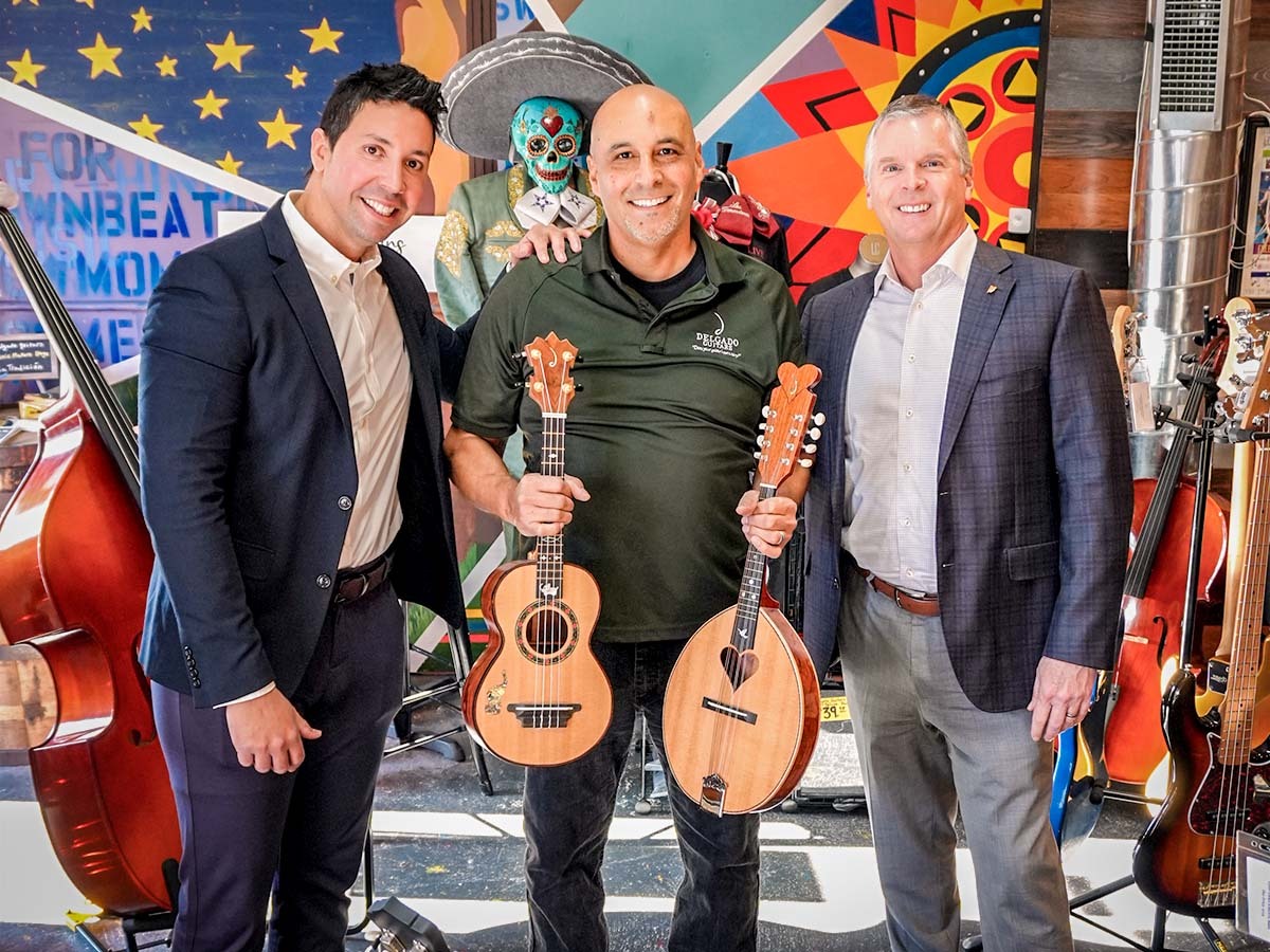 Darien Rizo, Manuel Delgado, and Chris Claybrook, pose with various string instruments in front of a mural.