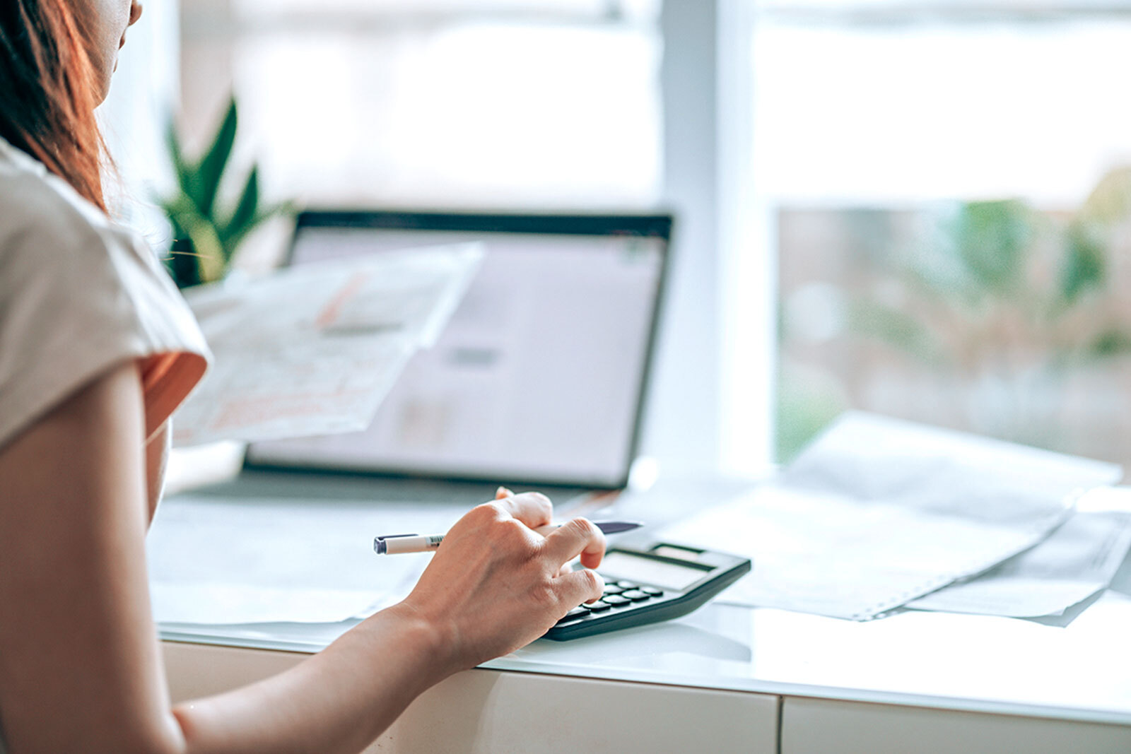 Person doing taxes at a desk with a calculator, documents, and an open laptop.