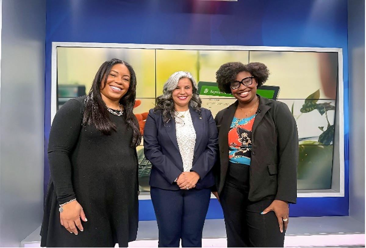 Three women in front of a large screen in a news studio.