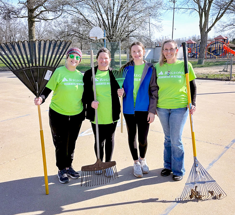Group photo of Regions associates holding yard tools, volunteering.