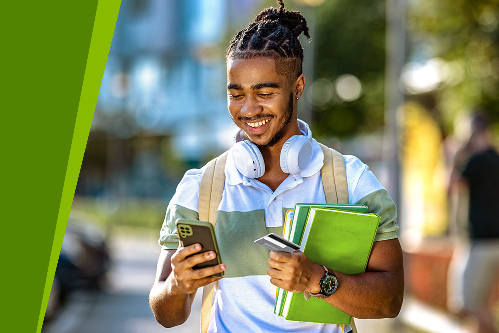 Young male with smartphone and credit card holding school books.