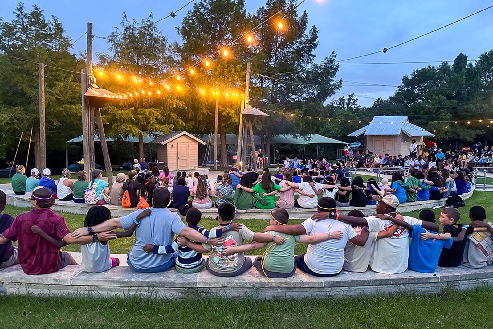 Camp For All attendees sitting around campfire holding arms.