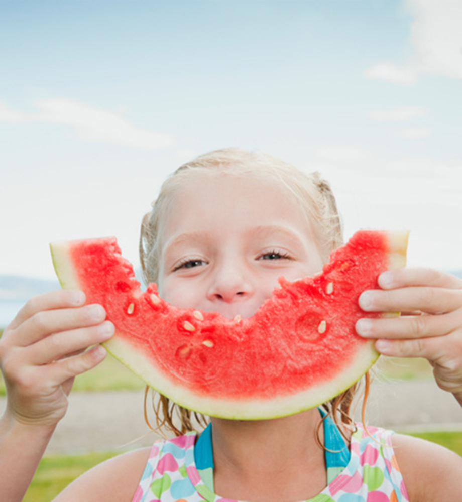 Young girl holding watermelon slice in front of her mouth.