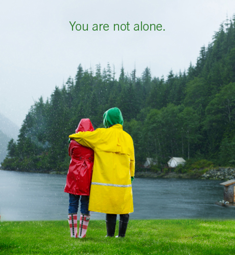 People in bright raincoats standing facing lake in the rain. Text: You are not alone.