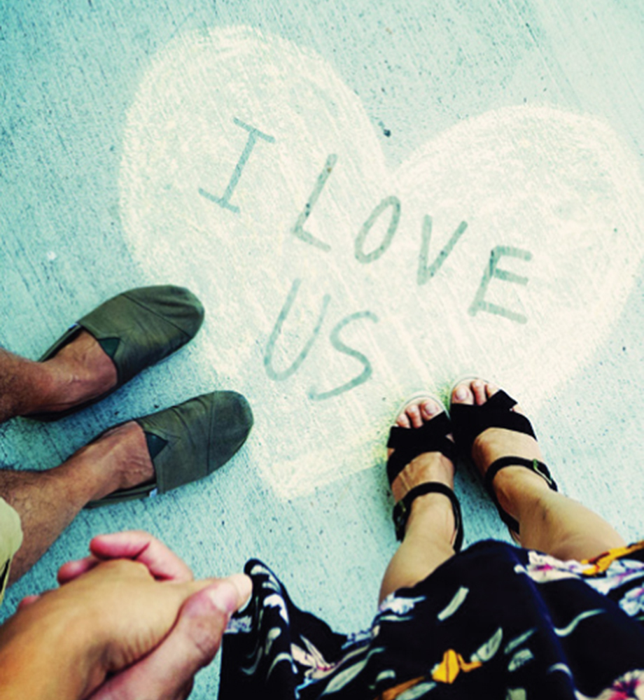 Couple holding hands and standing next to a heart that reads "I love us" in sidewalk chalk.
