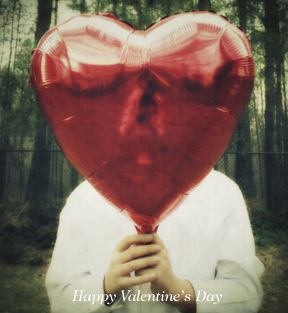 Person holding heart shaped balloon in front of their face. Text: Happy Valentine's Day.