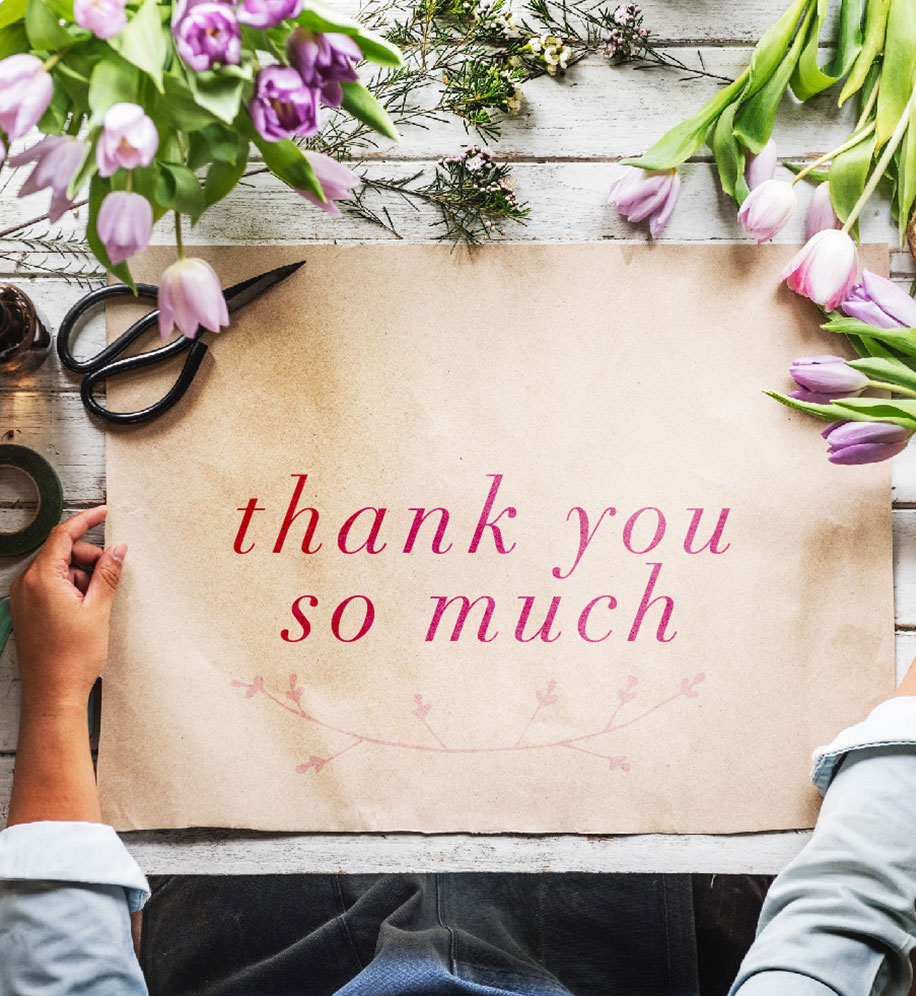 Person holding edges of kraft paper that's lying on table with flowers around it. Text: Thank you so much.